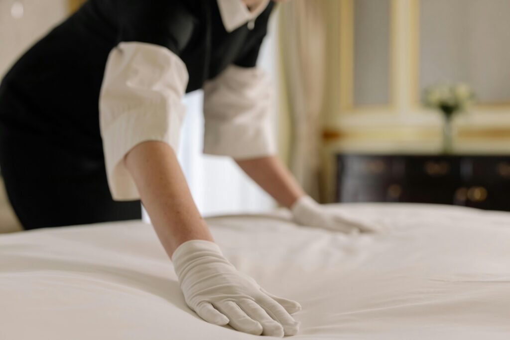 pexels-photo-6466479-6466479 A housekeeper straightening the bed linens in a well-appointed hotel room.