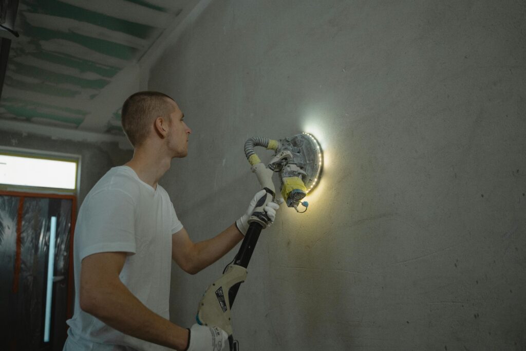 pexels-photo-6473978-6473978 Photo of a man using a power tool to sand a wall during an indoor home renovation project.