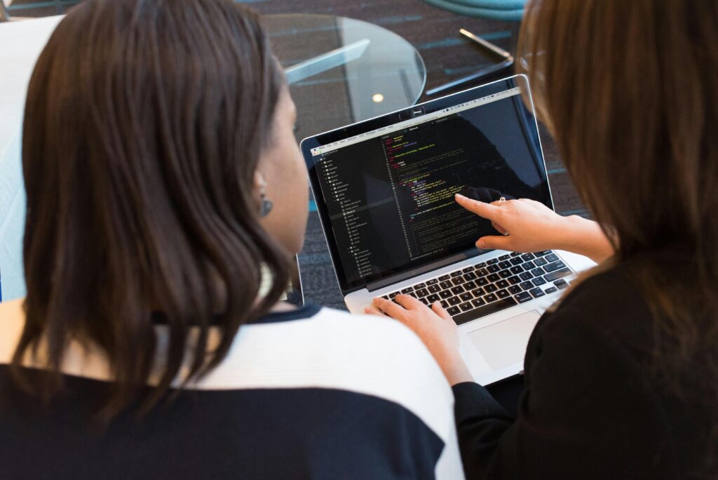 pexels-photo-1181263-1181263 Two women working together on software programming indoors, focusing on code.